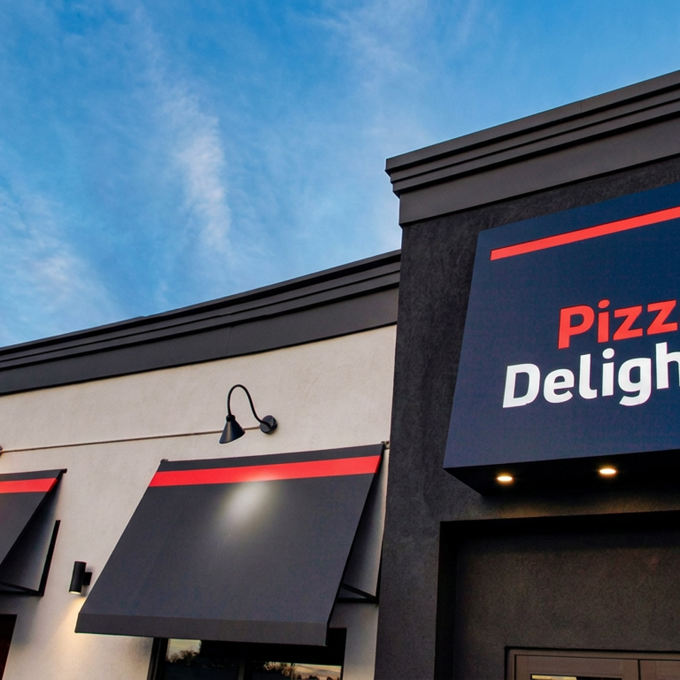 Pizza Delight restaurant exterior with black awnings, illuminated sign, and blue sky.